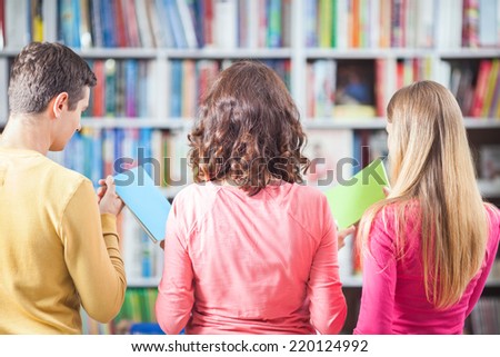 Rear view of three people choosing books from library or bookstore.