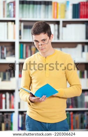 Young man reading a book in a library. Focus on foreground.