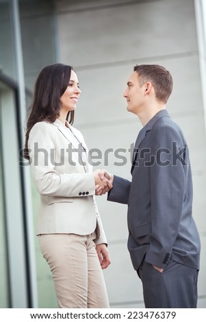 Businesswoman shaking hands with businessman in front of corporate office building