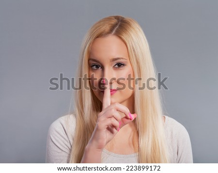 Portrait of pretty young woman holding finger on her lips. Studio shot, gray background.