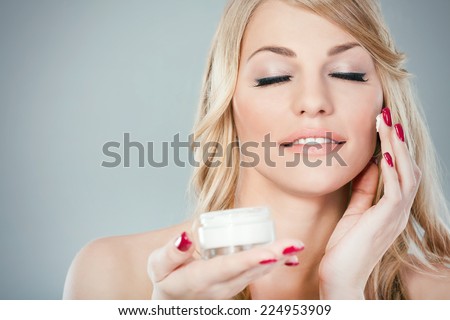 Beautiful young woman applying moisturizer on her face