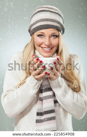 Beautiful blond woman having a cup of tea to warm up on a cold winter day. Studio shot.