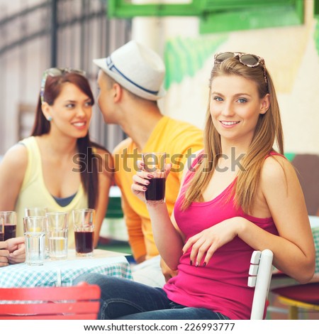 Young girl is sitting in a side-walk cafe with her friends and looking at camera