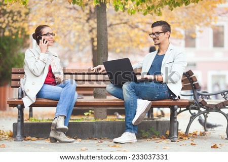 People sitting on a park bench. Woman talking on the mobile phone and man using laptop.