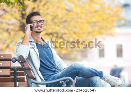 Young man sitting on the park bench talking on the phone