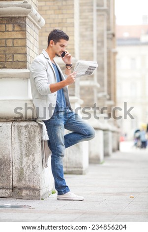 Young businessman reading newspaper and talking on the phone on the street
