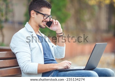 Businessman working on a laptop and talking on the phone while sitting on a park bench