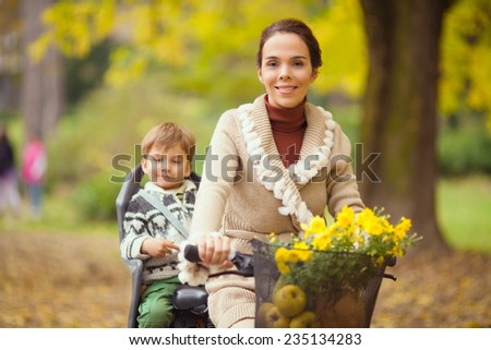 Beautiful mother riding a bicycle with her son sitting on the rear bike rack