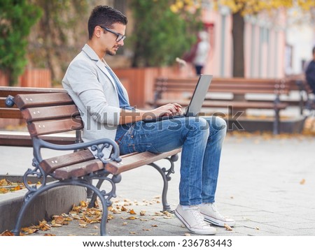 Young man sitting on the park bench with laptop on his lap