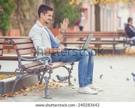 Young man sitting on the park bench and video-chatting on his laptop