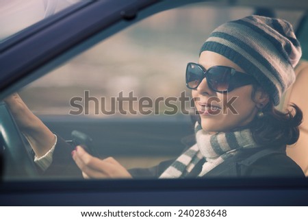 Smiling young woman driving a car and using mobile phone