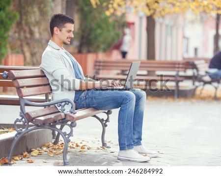 Young man sitting on the park bench with laptop on his lap