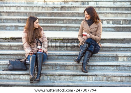 Two young women sitting on the stairs, talking and drinking coffee