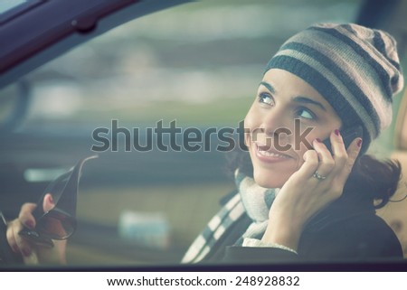 Smiling young woman driving a car and talking on the mobile phone