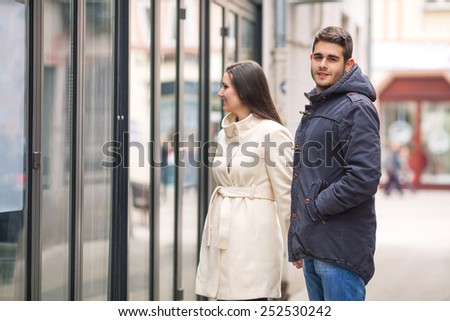 Couple in a walk. Girl looking at store window, young man looking at camera