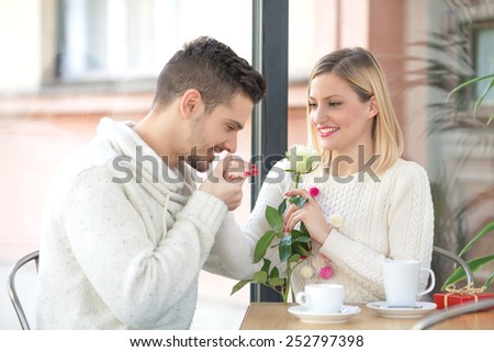 Romantic young man kissing hand of his girlfriend while she smelling a rose