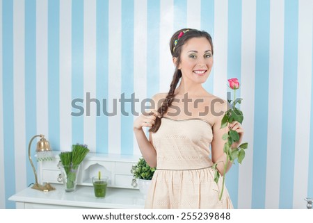 Portrait of smiling young woman holding a rose and standing in front of striped wallpaper.