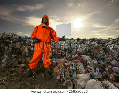 Recycling worker standing on the landfill and holding blank cardboard sign.