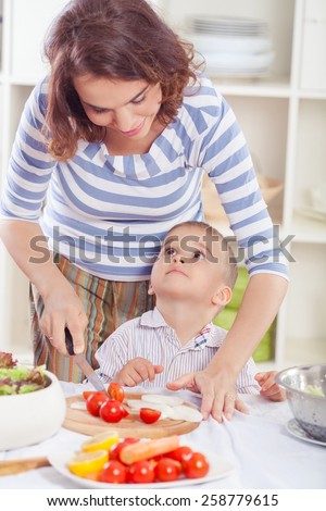 Cute little boy helping his mother in the kitchen with food preparation