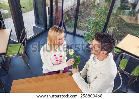 Romantic young man giving white rose to his girlfriend while sitting in a cafe
