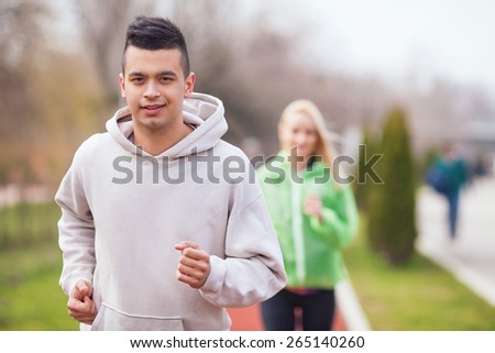 Handsome young man jogging on running track in a park. Unrecognizable woman jogging in the background.