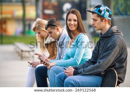 Portrait of smiling teenage girl hanging out with friends and using mobile phone