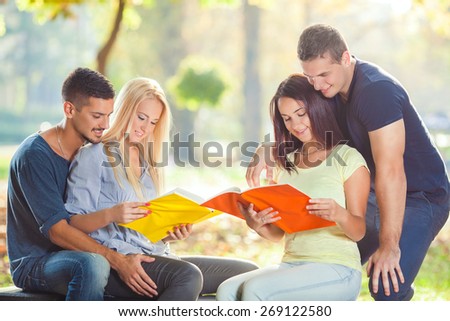 Group of four young students reading together in a park