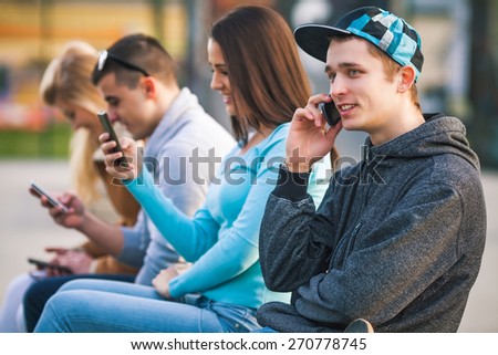Close-up of teenage boy talking on the phone while his friends using their mobile phones in the background