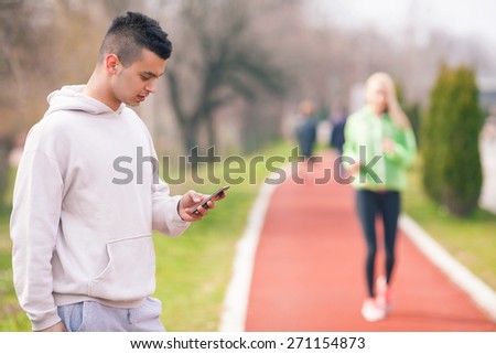 Focus on young coach measuring time for unrecognizable young woman running in the background