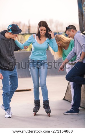 Group of teenagers helping their friend to learn to roller skate