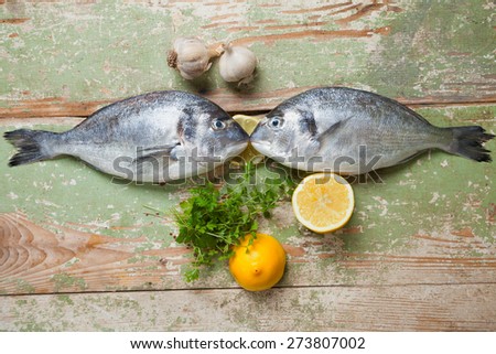Two fresh fishes lying on a wooden table with lemons, garlic and persley