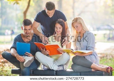 Group of four young students reading together in a park
