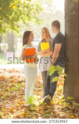 Three cheerful college students standing in a park talking