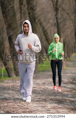Young man jogging in nature with young woman jogging behind him
