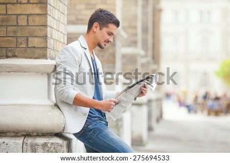 Young man reading newspaper on the city street