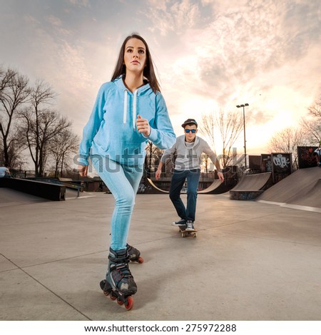 Teenage girl rollerblading in a skate park with a boy skateboarding in the background