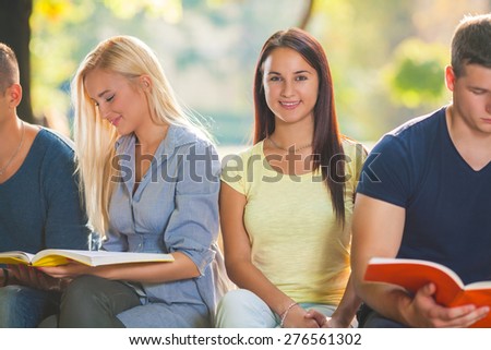 Portrait of smiling female college student sitting and studying with friends in a park