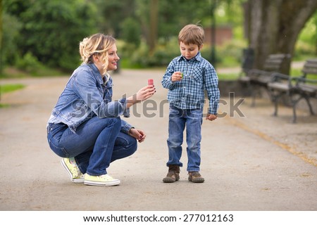 Cute little boy playing with his mother outdoors trying to make soap bubbles