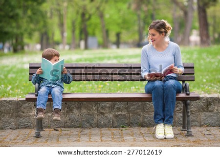 Young woman and cute little boy reading books in a park and talking