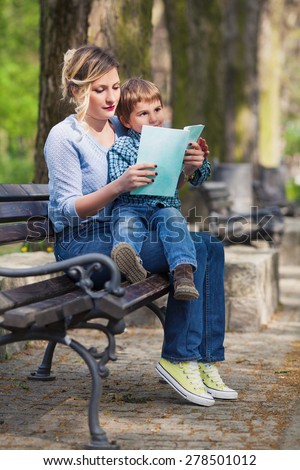 Mother sitting on a bench in a park and reading children??s stories to her son