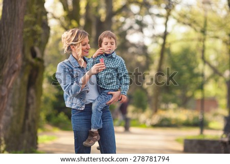 Young mother carrying her cute little son in her arms and helping him to make soap bubbles
