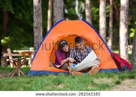 Young couple sitting in a tent reading maps and planning their camping adventure