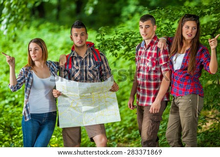 Confused young men with map looking at camera and confident young women showing them directions in the forest