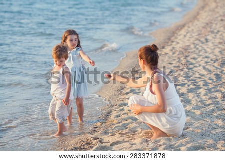 Two little children collecting seashells on the beach with their mother