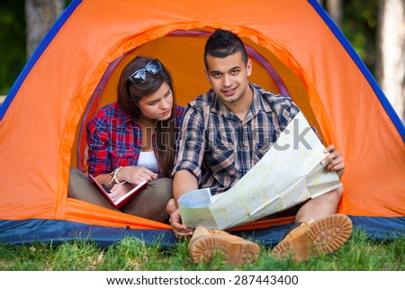 Portrait of young couple sitting in a tent reading maps and planning their camping adventure
