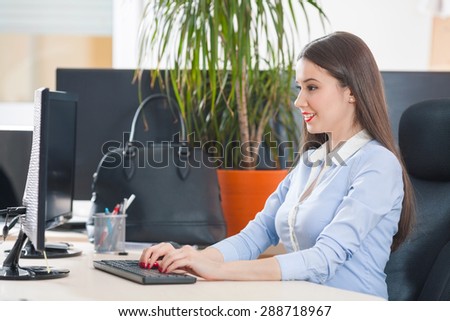 Portrait of attractive young businesswoman sitting at her desk in an office typing on computer keyboard