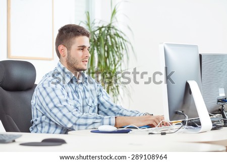 Portrait of smiling young businessman typing on computer keyboard and looking at computer monitor