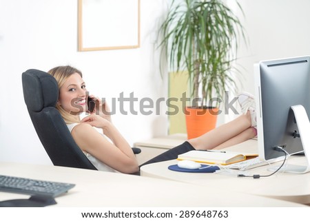 Young businesswoman talking on the phone in an office with her foot on the desk