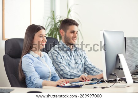 Portrait of cheerful young businesspeople typing on computer keyboard and looking at computer monitor