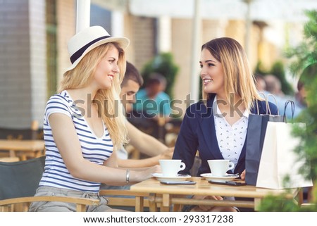 Two young girlfriends sitting in a cafe chatting and relaxing after successful shopping